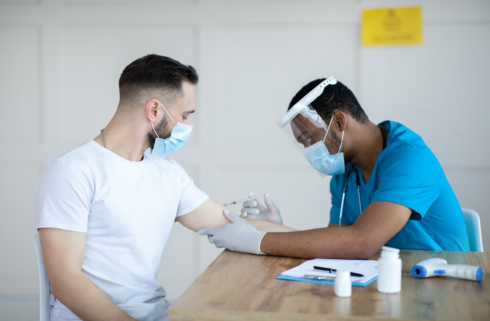 Young guy receiving injection of covid-19 vaccine at clinic. Black doctor immunizing male patient